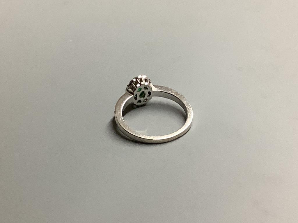A modern 18ct white gold, emerald and diamond set oval cluster ring, with diamond set shoulders, size L, gross weight 3.4 grams.